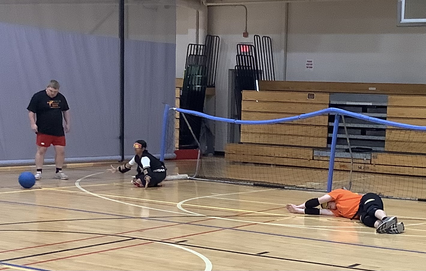 Athlete diving to defend the goalball net, wearing eyeshades and in defensive position on the court